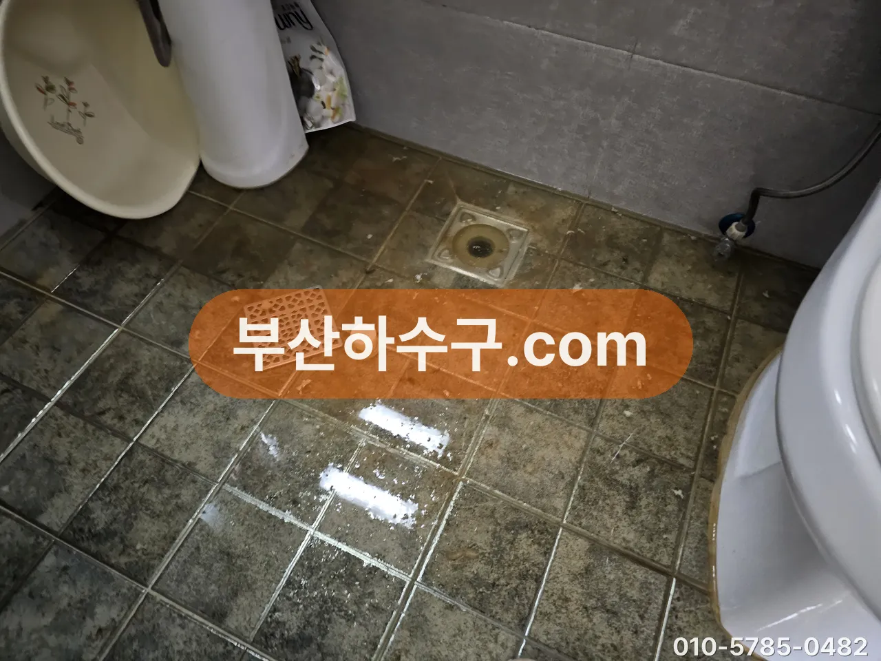 욕실 바닥 유가 두 개 주변에 물이 얇게 고인 상태, 봉수가 마른 배수구인지 확인하는 장면