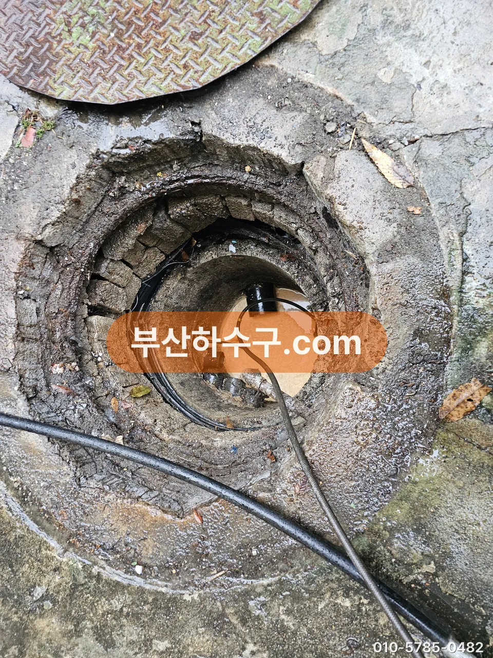 보도 맨홀 뚜껑을 열고 준설·세척 호스를 관 안으로 내린 장면