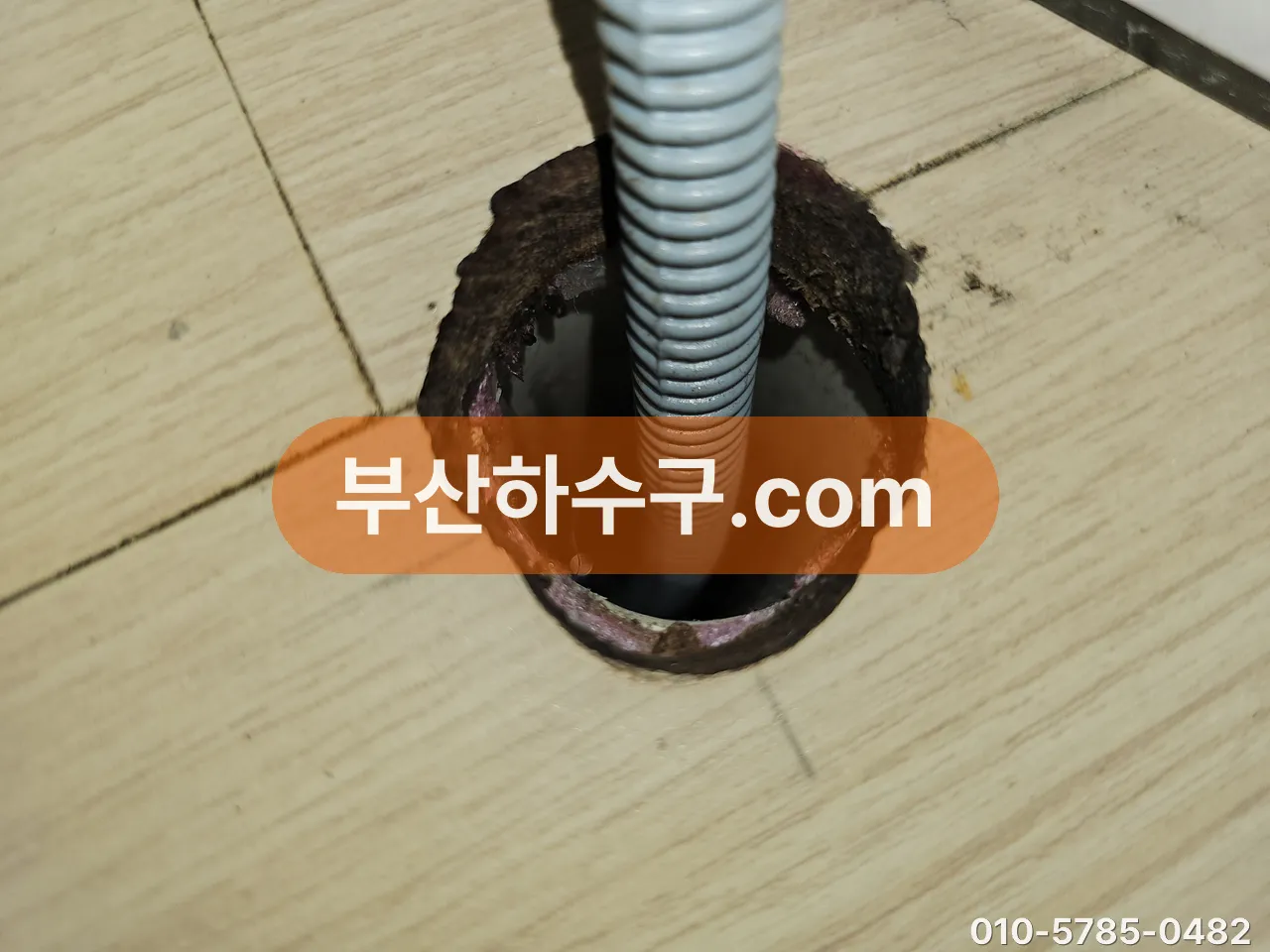 바닥 매립 배수관 입구에 에어컨 드레인 호스를 꽂아 배출을 확인하는 장면