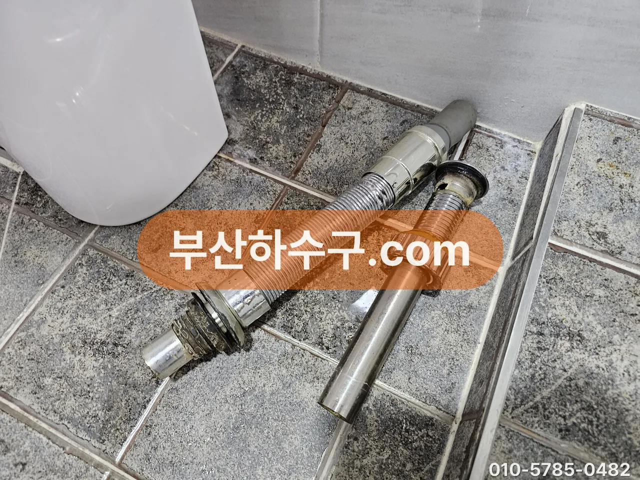 세면대 아래에서 떼어낸 낡은 팝업·배수관·트랩 부속을 바닥에 늘어놓은 모습